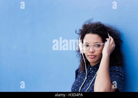 Thoughtful young woman listening music against blue background Stock Photo