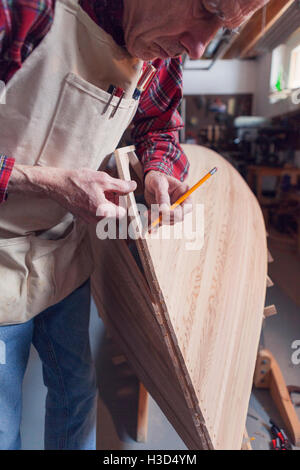 Senior man using pencil on wooden boat in workshop Stock Photo