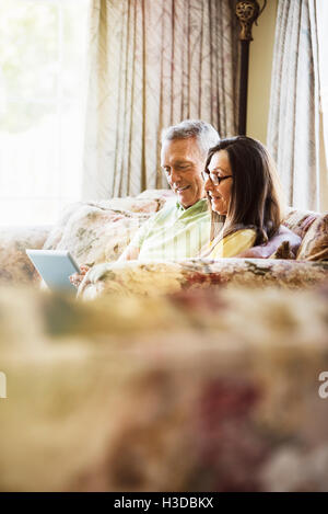 Smiling senior couple sitting on a sofa, using a laptop computer. Stock Photo