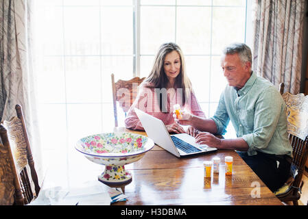 Senior couple sitting at a dining table, looking at a laptop computer. Stock Photo