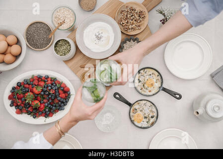 Breakfast fruit, berries and yoghurt, eggs and cooked omelettes. Two people reaching to dish out food. Stock Photo