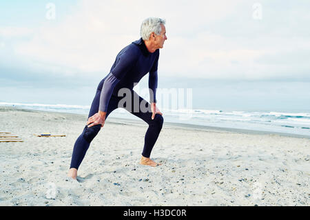 Senior man wearing wetsuit standing on a sandy beach. Stock Photo