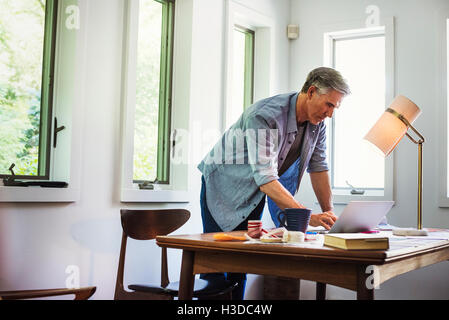 A man at home using a laptop on a desk. Stock Photo