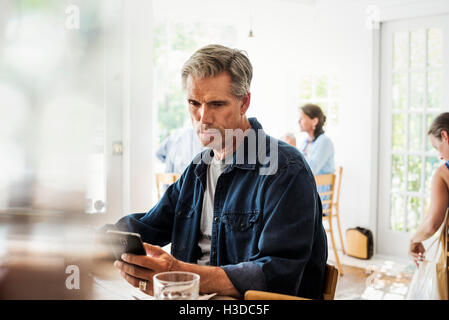 Man sitting in a coffee shop looking at his smart phone. Blurred foreground. Stock Photo