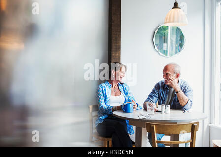 Two people seated at a coffee shop table.  Blurred foreground. Stock Photo