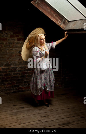 Young woman in vintage dress in attic with brolly Stock Photo
