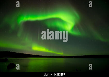 Northern Lights in Starry Sky - Bright northern lights rolling over the starry night sky over a lake. Stock Photo