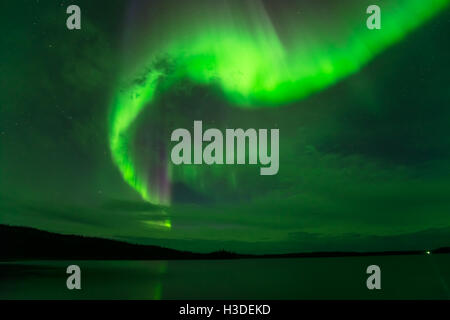 Northern Lights in Cloudy Sky - Bright northern lights shining through cloudy night sky over a lake. Stock Photo