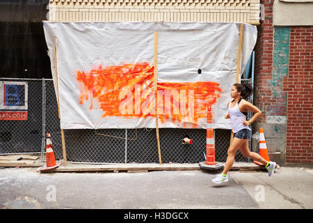 A young asian woman runs by a construction site on a city street. Stock Photo