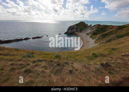 Looking towards a large rock outcrop on one end of a natural bay formed in the soft chalk with a shingle beach on a sunny day. Stock Photo