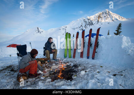 Snowboarders hanging out around a fire during sunset at base camp Stock Photo