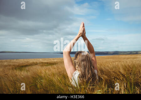 Woman with hands raised over head in prayer position in field Stock Photo