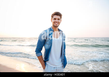 Happy young man in jeans shirt standing and smiling on the beach Stock Photo