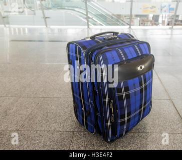 Large, comfortable suitcase on wheels with extendable handle made of a beautiful checkered fabric. Standing on the floor in the Stock Photo