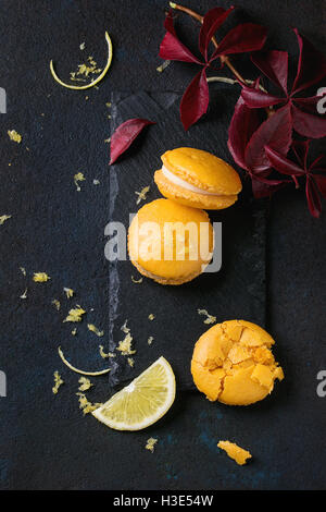 Whole and broken orange lemon homemade macaroons with white chocolate, lemon slice and zest, citrus sugar on slate board with au Stock Photo