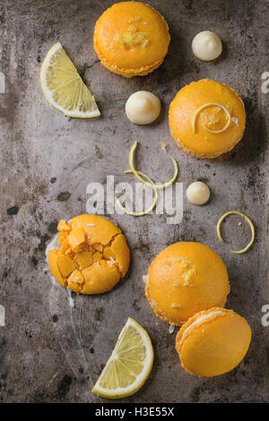 Whole and broken orange lemon homemade macaroons with chopped white chocolate and citrus sugar and zest over old metal textural  Stock Photo
