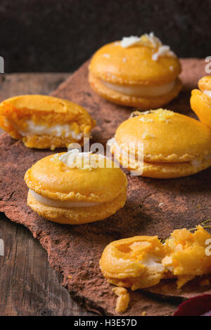 Whole and broken orange lemon homemade macaroons with white chocolate and citrus sugar and zest on old clay board with autumn re Stock Photo