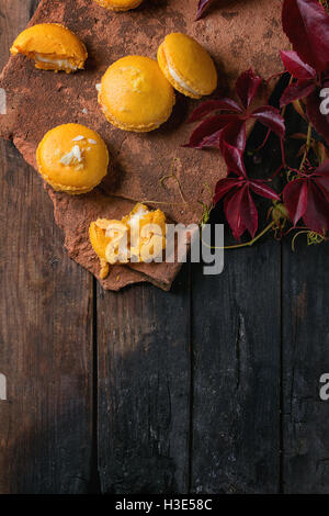 Whole and broken orange lemon homemade macaroons with white chocolate and citrus sugar and zest on old clay board with autumn re Stock Photo