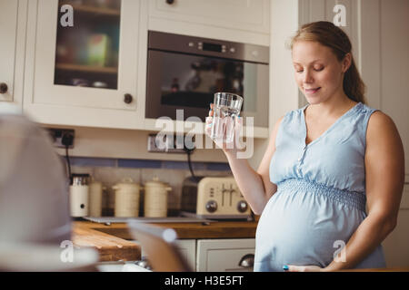 Pregnant woman drinking water in kitchen Stock Photo