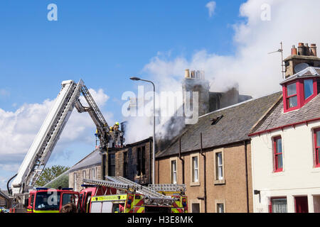 Scottish Fire and Rescue Service firefighters up a ladder tackling a burning house roof. Elie and Earlsferry Fife Scotland UK Stock Photo