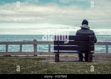 Man sitting on bench overlooking sea Stock Photo