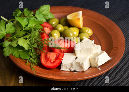 feta cheese, tomatoes, olives and herbs in a clay plate - Greek lunch