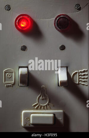 Details of an old dirty plastic switches for bathroom, red light is on for boiler. Stock Photo