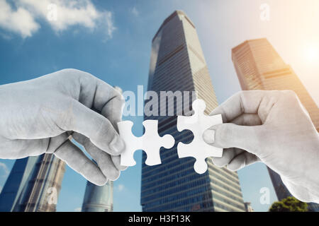 Hands putting partnership puzzle pieces together on skyscraper building in background. Partnership network concept Stock Photo