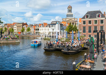 Hartebrugkerk church tower, boats and people on outdoor terrace of cafe on Rhine canal in Leiden, South Holland, Netherlands Stock Photo