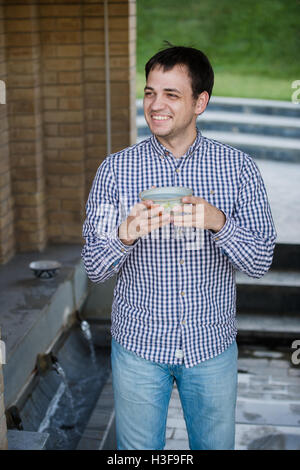 Portrait of young happy smiling man drinking water from spring, outdoors Stock Photo