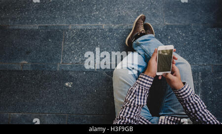 young Man with the phone in his hand sitting on the steps. top view Stock Photo