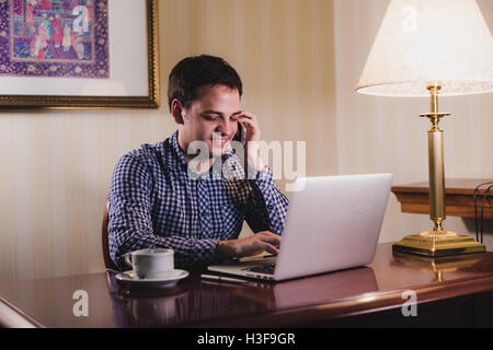 Casually dressed young businessman using mobile phone and laptop. Stock Photo
