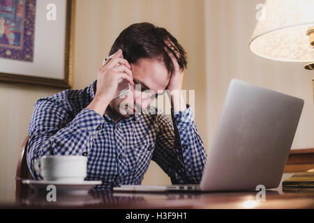 tired man with laptop and coffee having a work call on his phone, businessman in office or home Stock Photo