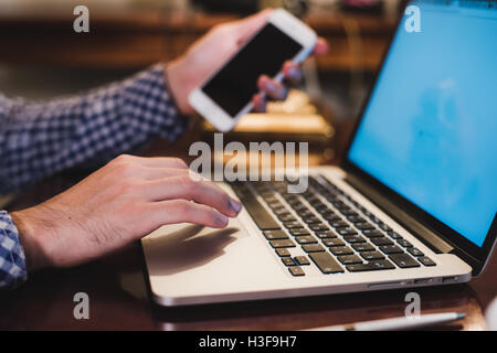 Close up male hands holding big smart phone while connecting to wireless, businessman using technology sitting at wooden desk Stock Photo