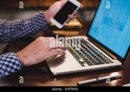 Close up male hands holding big smart phone while connecting to wireless, businessman using technology sitting at wooden desk Stock Photo