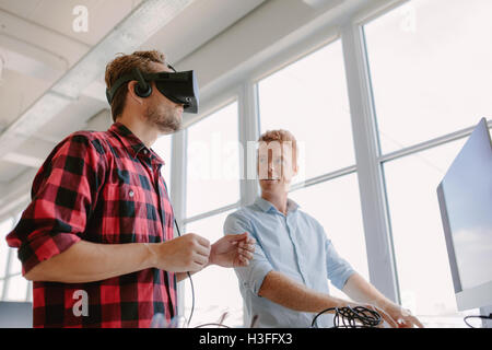 Shot of two young men testing virtual reality headset. Business men in office testing VR glasses. Stock Photo
