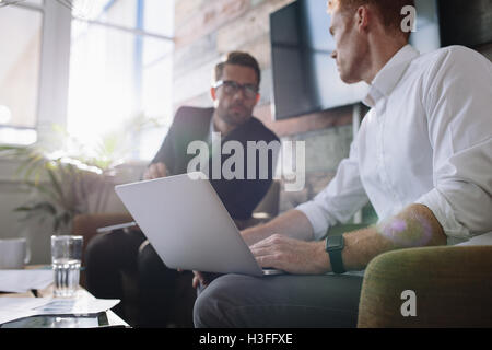 Two young man sitting in office and discussing business. Businessman with laptop talking with colleague during meeting. Stock Photo