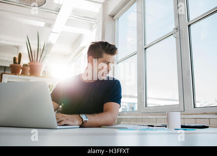 Shot of young businessman working on at his desk, using laptop and looking at documents on table. Stock Photo