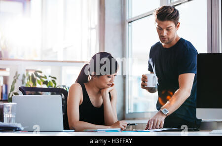 Shot of asian businesswoman sitting at her desk with male colleague helping her with new business ideas. Two young executive wor