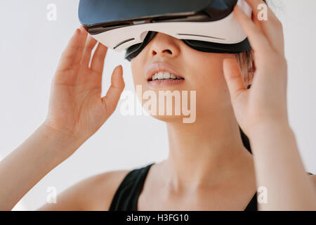 Close up of happy young woman using the VR goggles against grey background. Asian female model wearing virtual reality headset. Stock Photo