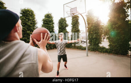 Young man taking shot with friend blocking on basketball court. Streetball players on court playing basketball. Stock Photo