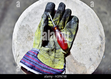 Dirty worker's glove holding a screwdriver on a wooden plank in a workshop Stock Photo