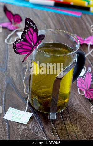 Background decoration paper butterflies in a glass of mint tea. Peppermint tea, cardboard, colored paper and felt-tip pens on a Stock Photo
