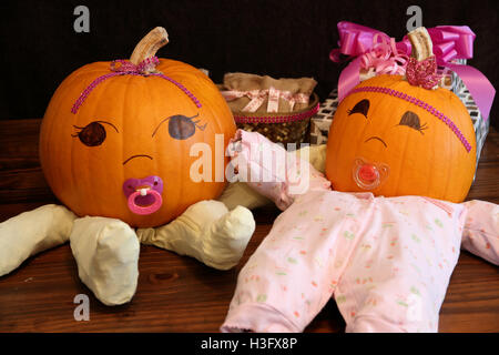 Two pumpkins dressed up as princess babies with pacifiers on a table beside gifts. Stock Photo