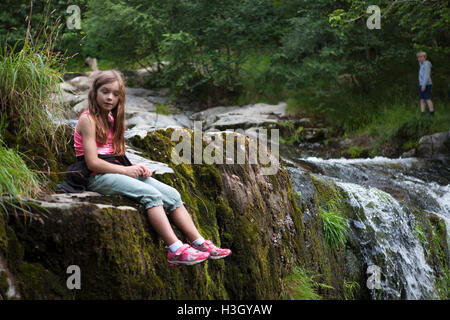 Young girl sits by High Force, a waterfall on Aira Beck, Lake District, Cumbria, England Stock Photo