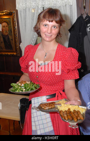 A waitress dressed in traditional Bavarian dress the famous Nuremberg Bratwurst (Nuremberg sausage) and potato salad served on a metal plate in the Stock Photo