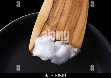 Coconut oil on wooden spatula over teflon pan. Also copra oil, an edible oil, extracted from the kernel of meat of coconuts. Stock Photo