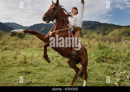 Kazakh horse rider raising arm on rearing gelding in Huns village Kazakhstan Stock Photo