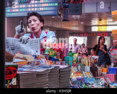 a japanese woman with a  newspaper pointing her finger, a worker at a retail stall in shibuya railway station, tokyo japan Stock Photo