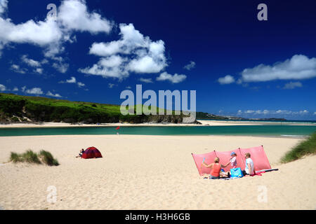 A family sitting on a sandy beach with turquoise sea with deep blue sky and white clouds. Stock Photo